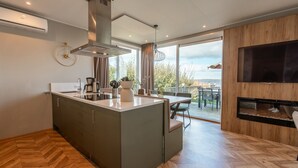 A modern kitchen with a central island, a built-in stove, and a large window overlooking a deck. - De Wiedense Meren - Villa Waterrijk MIVA | 3p (Wanneperveen)