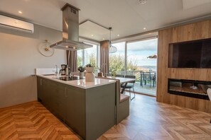 Ett modernt kök med en central köksö, en inbyggd spis och ett stort fönster med utsikt över en terrass.