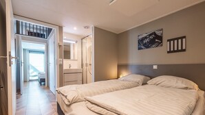 A bedroom with two beds, a bathroom, and a staircase leading to an upper level.