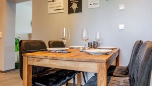 A dining area with a wooden table set for four, black upholstered chairs, and framed wall art. - Vacation apartment Anna at the gateway to the Eifel National Park (Heimbach/Eifel) (Heimbach)
