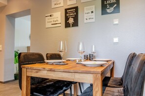 Ein Essbereich mit einem Holztisch, gedeckten Plätzen für vier Personen, schwarzen Polsterstühlen und Wandbildern in Rahmen.