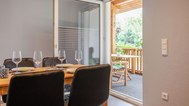 A dining area with a table set for four, a sliding glass door leading to an outdoor patio, and a wooden deck visible through the door. - Vacation apartment Anna at the gateway to the Eifel National Park (Heimbach/Eifel) (Heimbach)