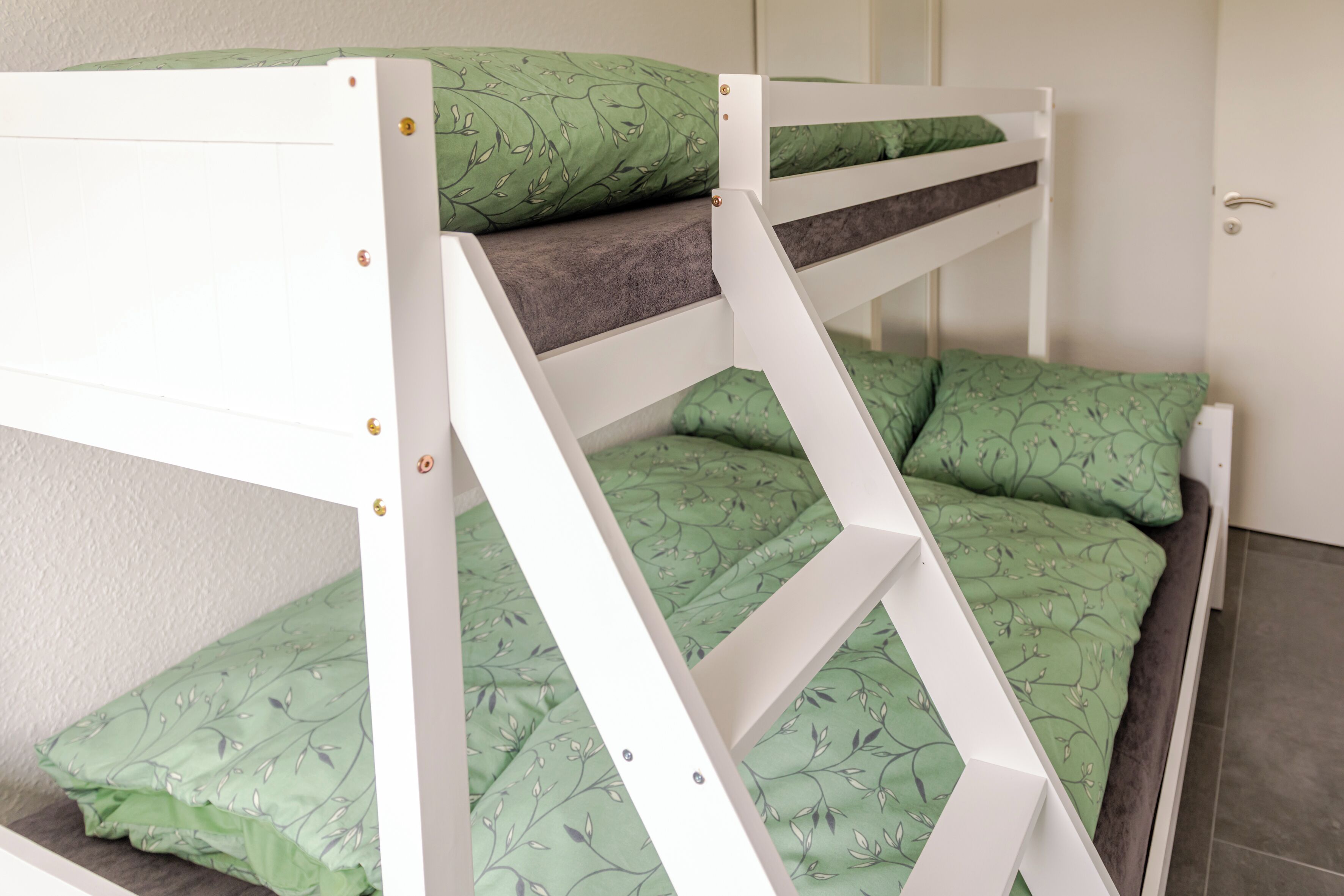 A bunk bed with green bedding and a white frame.