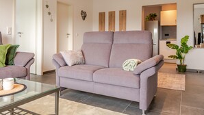 A modern living room with a sofa, a glass coffee table, and a kitchen area in the background. - Vacation apartment Anna at the gateway to the Eifel National Park (Heimbach/Eifel) (Heimbach)
