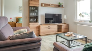 A modern living room with a sofa, TV, wooden cabinet, and a glass coffee table. - Vacation apartment Anna at the gateway to the Eifel National Park (Heimbach/Eifel) (Heimbach)