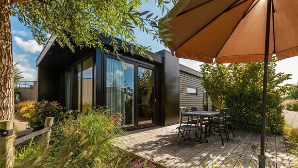 A modern outdoor patio with a wooden deck, a table with chairs, and a large umbrella. - De Wiedense Meren - Rietland Lodge | 4p (Wanneperveen)