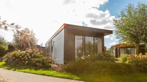 A modern building with a glass facade, surrounded by lush greenery and a clear sky. - De Wiedense Meren - Rietland Lodge | 4p (Wanneperveen)