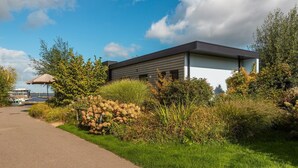 A modern building with a pathway leading to it, surrounded by lush greenery and a clear sky. - De Wiedense Meren - Rietland Lodge | 4p (Wanneperveen)