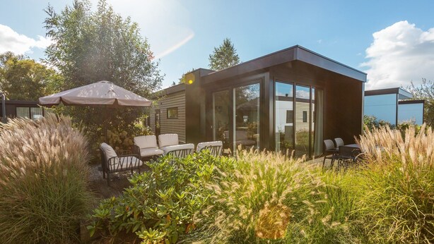 Una casa moderna con un patio, mobiliario exterior y una sombrilla grande.