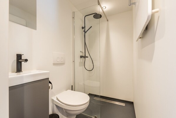 A modern bathroom with a glass-enclosed shower, a toilet, and a sink with a faucet.