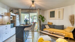 Una cucina moderna con isola centrale, zona pranzo con uno sgabello da bar, divano con cuscini e un'ampia finestra.