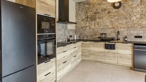 A modern kitchen with a stone wall, a black refrigerator, wooden cabinets, and a built-in oven.