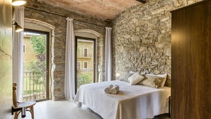 A bedroom with a stone wall, a bed with white bedding, and a balcony with curtains.