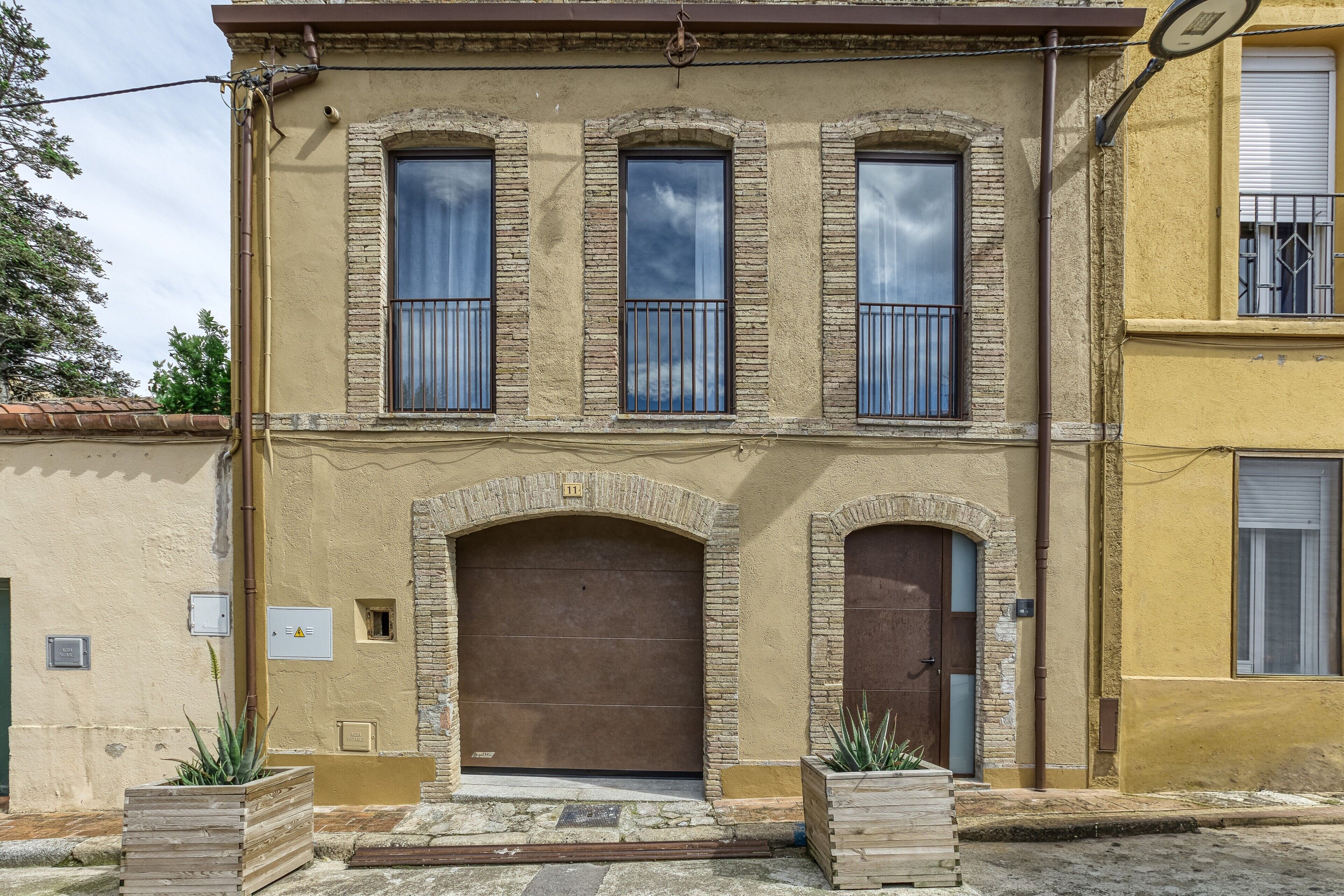 A two-story building with a brown door and windows, a small balcony, and a stone facade.