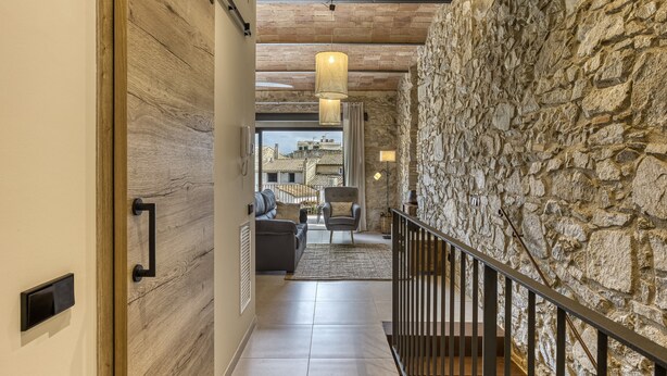 A hallway with a stone wall, a wooden door, a staircase, and a view of the outside.