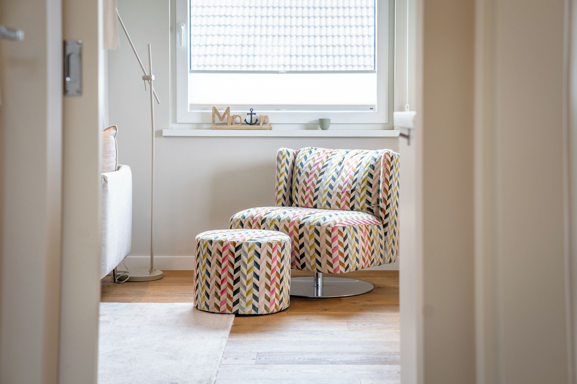 Una stanza con una finestra, un termosifone, una lampada da terra e due pouf con motivo a zig-zag.