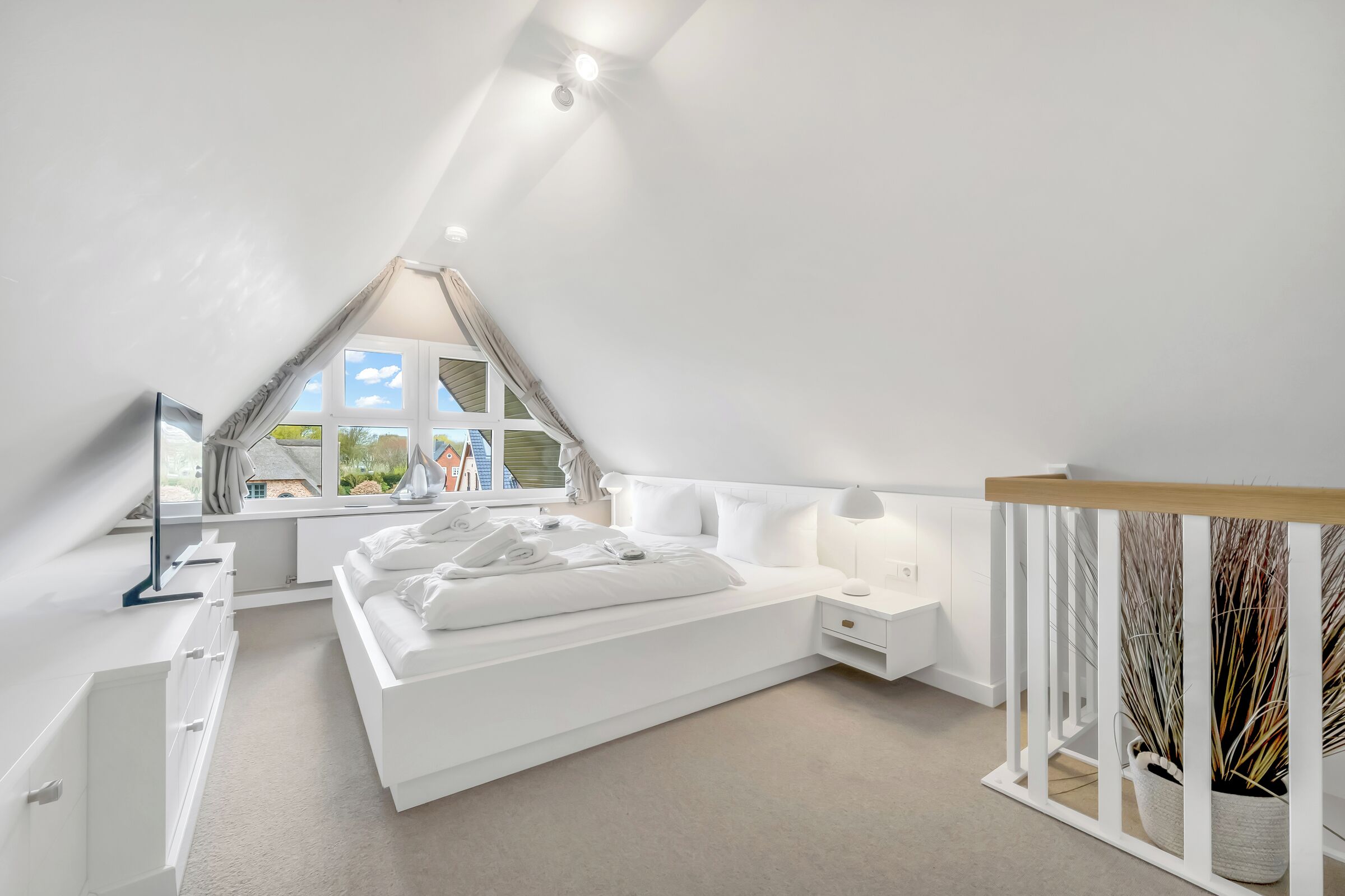 A modern bedroom with a sloped ceiling, a large bed, bedside tables, and a view of the outside.