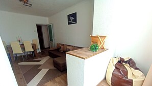 Olohuoneessa on sohva, sohvapöytä, ruokailutila tuoleineen sekä pieni kasvi puutelineellä.
