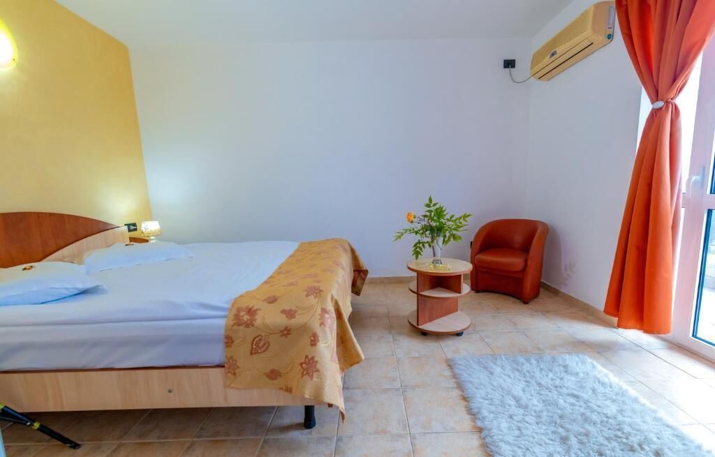 Un dormitorio con una cama, una silla, una mesita con una planta y una ventana con cortinas.