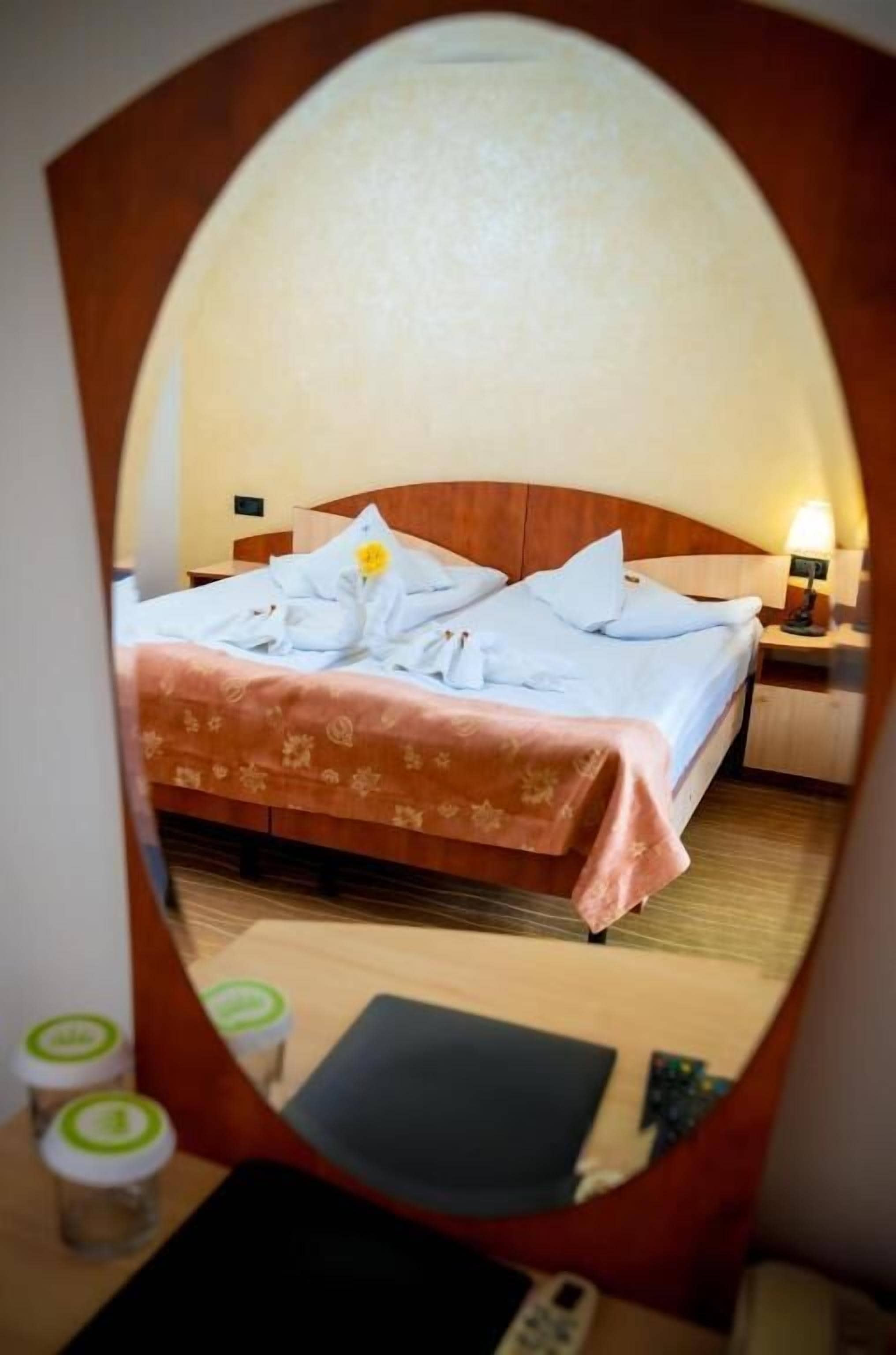 Een hotelkamer met een bed, nachtkastje, lamp en een spiegel die de kamer weerspiegelt.