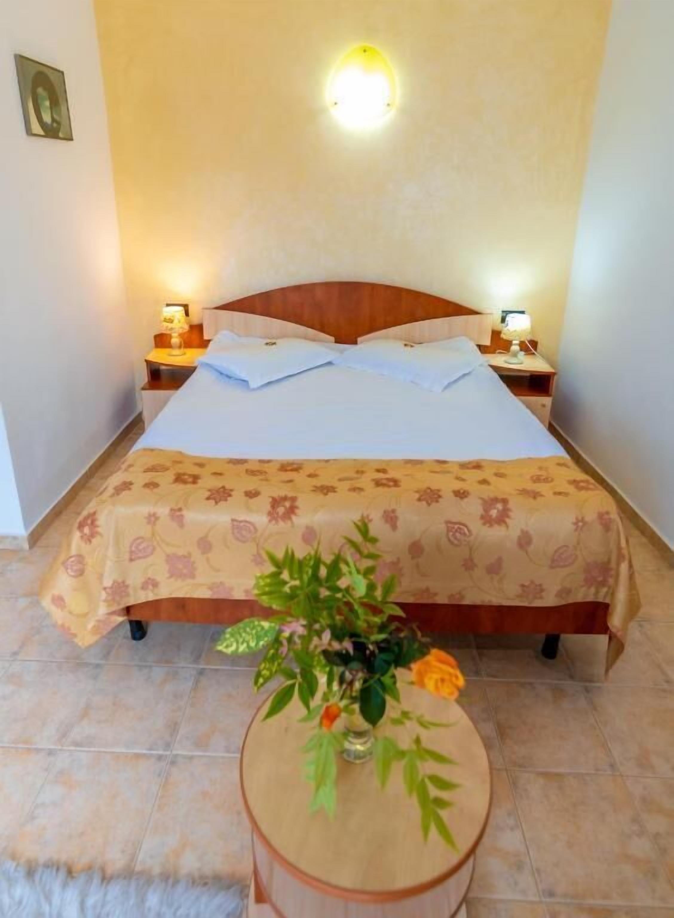 Une chambre d’hôtel avec un lit, des lampes de chevet, une petite table avec un vase et un luminaire fixé au mur.