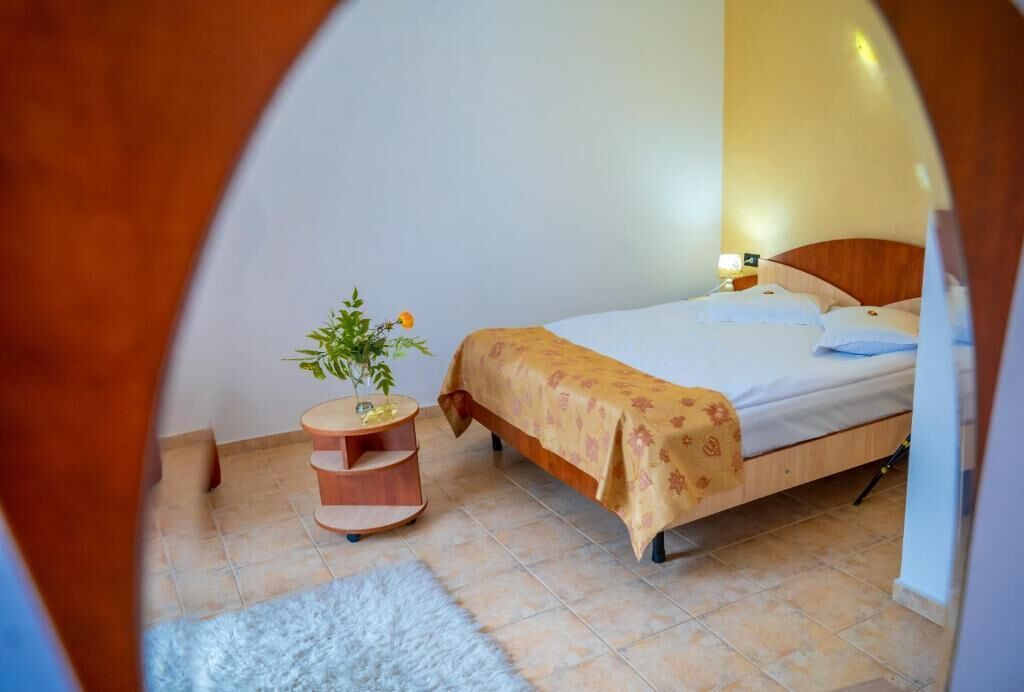 Un dormitorio con una cama, una mesita de noche, una planta pequeña y una alfombra blanca.