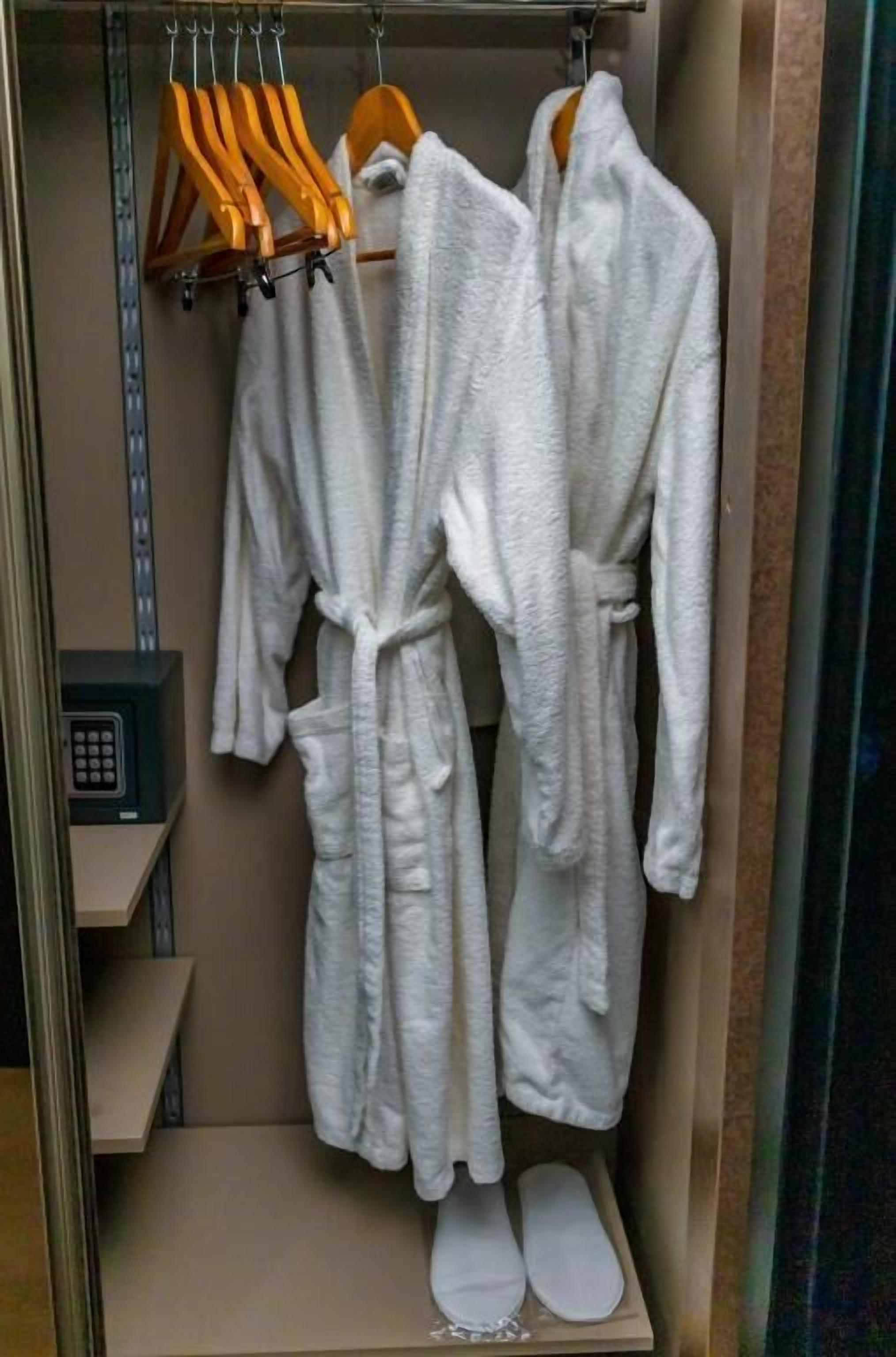 A bathroom with a white robe hanging on a rack, a pair of slippers on a shelf, and a small electronic device on a shelf.