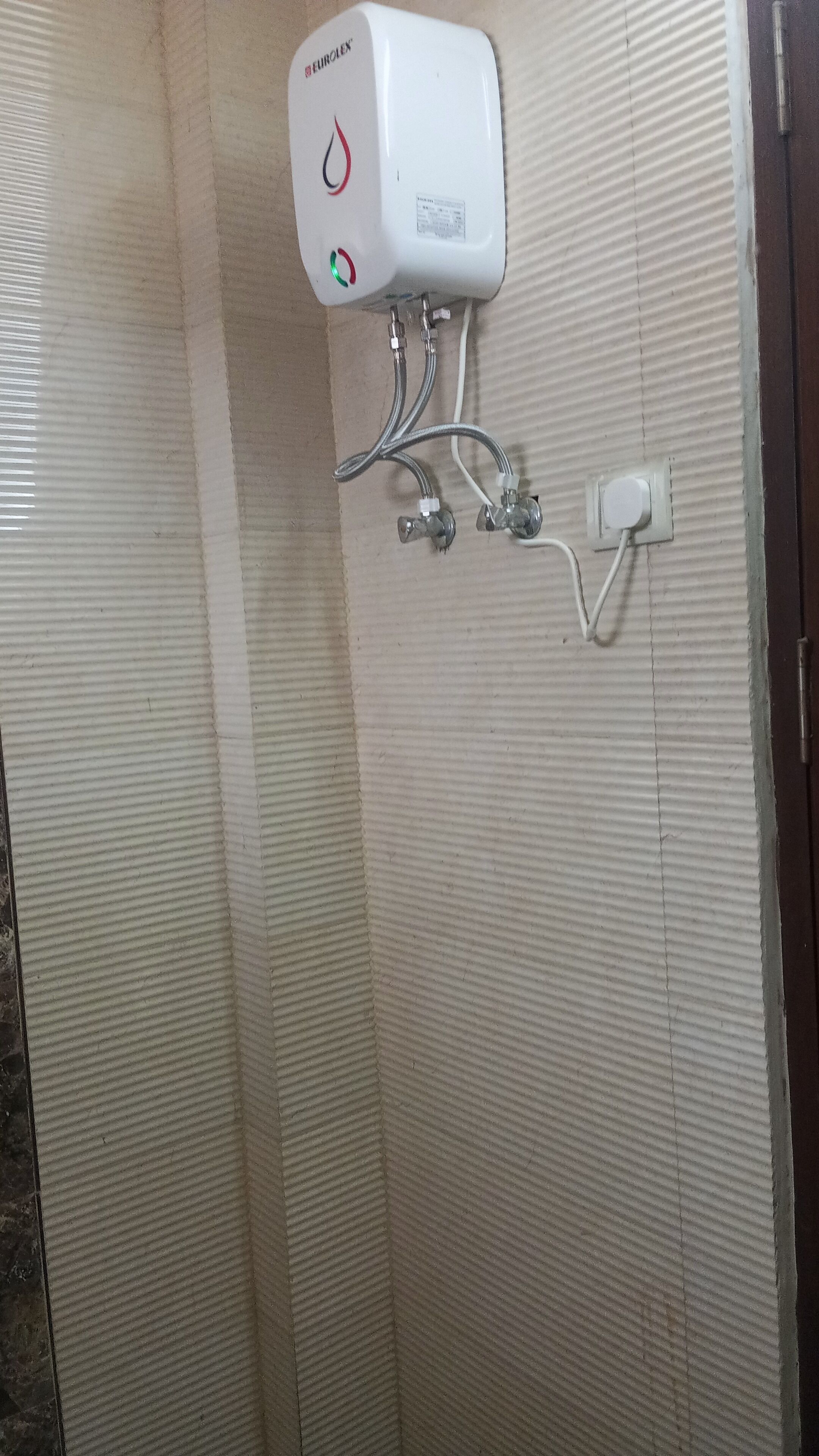 A bathroom with a hand dryer mounted on the wall, a towel rack, and a showerhead.