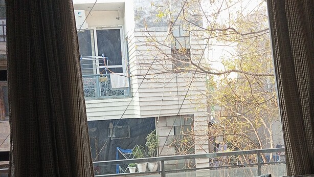 Una habitación con ventana, radiador, sof á y vista a un edificio.