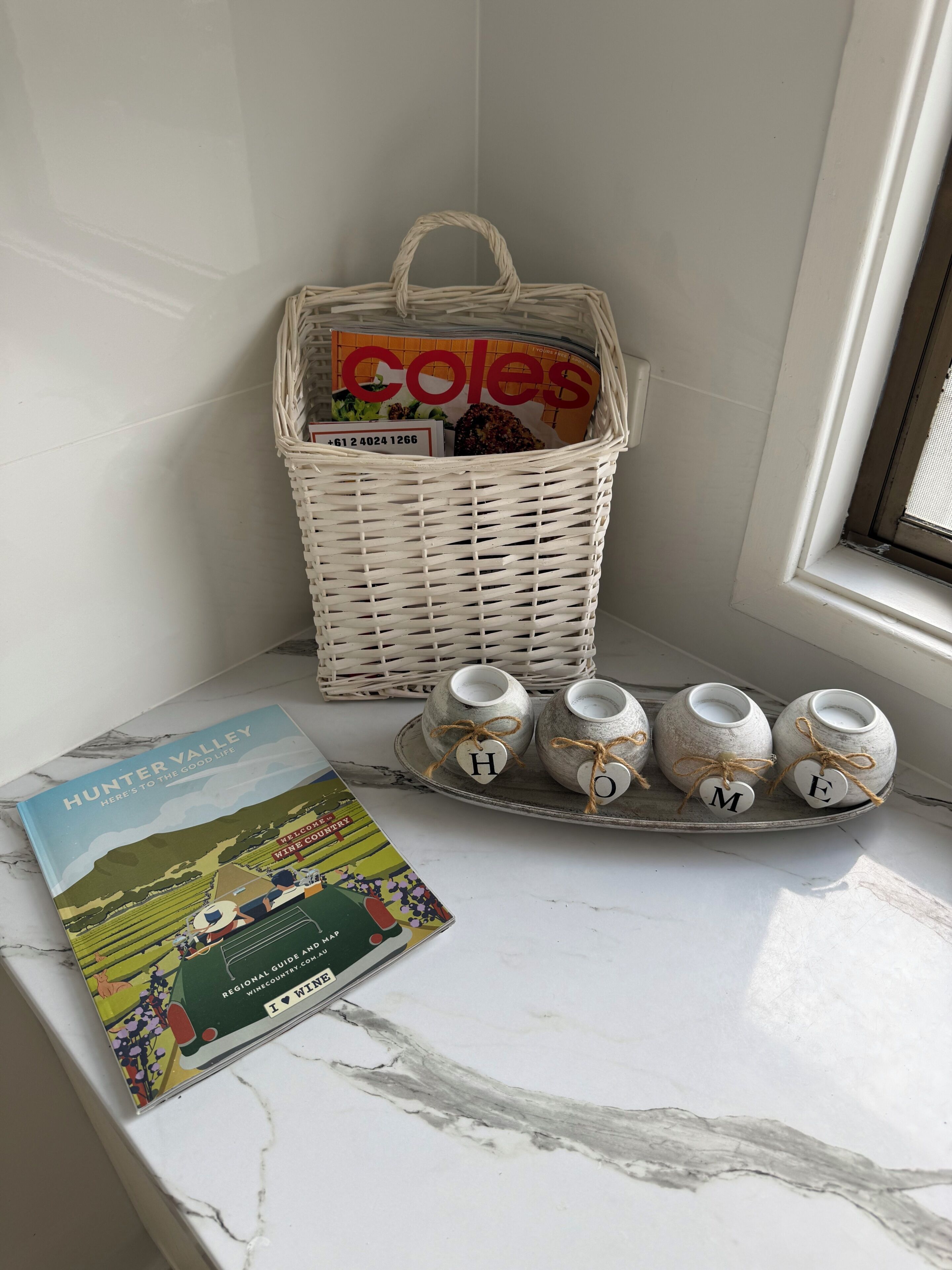 A wicker basket with a magazine, a tray with ceramic mugs, and a book on a marble surface.