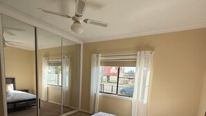 Ein Schlafzimmer mit Bett, Deckenventilator, Fenster mit Vorhängen und einer Schiebetür.