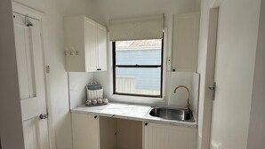 Eine kleine Küche mit weißen Schränken, einem Fenster, einer Spüle und einem Fliesenboden.