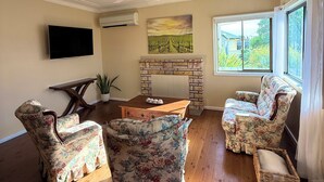 Ein Wohnzimmer mit Kamin, blumigen Sesseln, einem Holztisch und einem Fernseher an der Wand.
