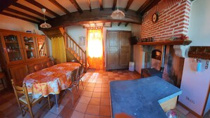 Una cocina rústica con una mesa de comedor, sillas, una chimenea y una escalera que lleva a otra habitación.