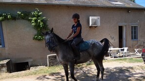 Una persona montando a caballo en un espacio al aire libre, con un edificio al fondo.