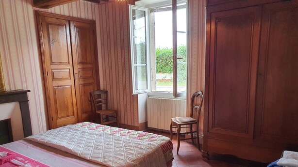 Una habitación con una cama, dos sillas de madera, un ventanal y un radiador.