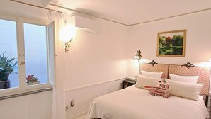 Une chambre à coucher comprenant un lit, des tables de chevet, une fenêtre avec des rideaux, un climatiseur fixé au mur et un tableau.