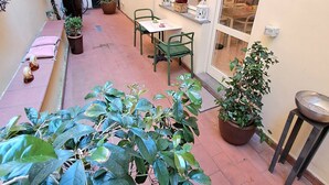 Une petite cour intérieure avec une table et des chaises, des plantes en pot et une fenêtre donnant sur l’intérieur.