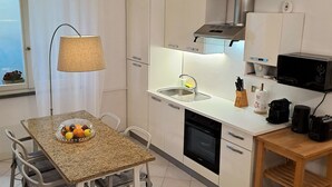 Une cuisine compacte comprenant une table à manger, des chaises, un panier de fruits, un évier, une cuisinière, un four à micro-ondes et une machine à café.
