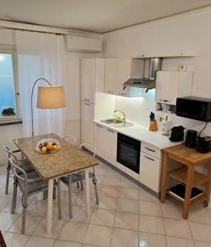 A compact kitchen with a dining table, chairs, a fruit bowl, a sink, a stove, a microwave, and a coffee maker. - Apartment in the historic center of Lucca near the Cathedral San Martino (Lucca)