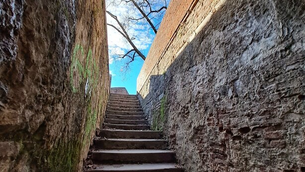 Un escalier en pierre menant vers le haut, à travers un étroit passage, avec un ciel bleu dégagé visible au-dessus.