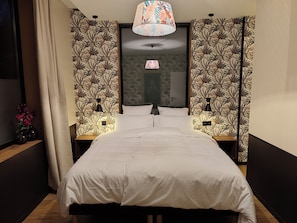 Ein Hotelzimmer mit einem großen Bett, zwei Nachttischen, einer Ablagefläche und einer Wandleuchte, sowie einem Fenster mit Vorhängen.