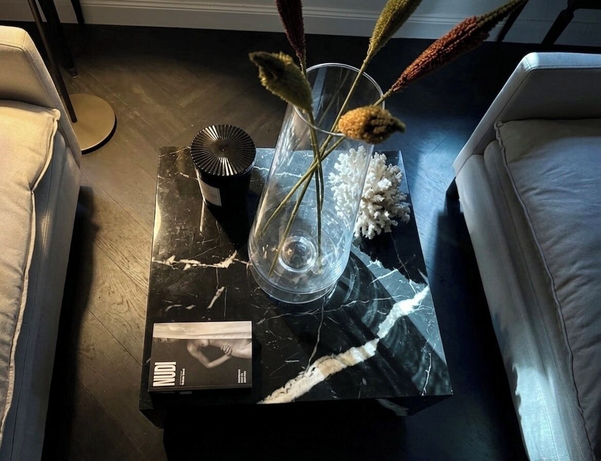 A black marble coffee table with a clear vase containing dried flowers, a book, and a decorative item.