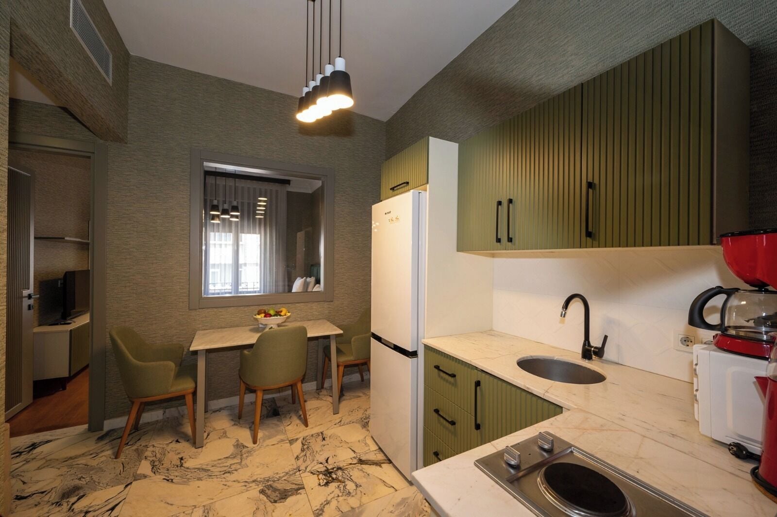 A compact kitchen with a dining area, a refrigerator, a sink, and a coffee maker.