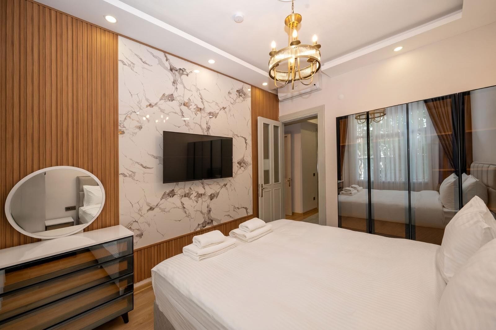 A modern bedroom with a bed, a TV, a mirror, and a chandelier.
