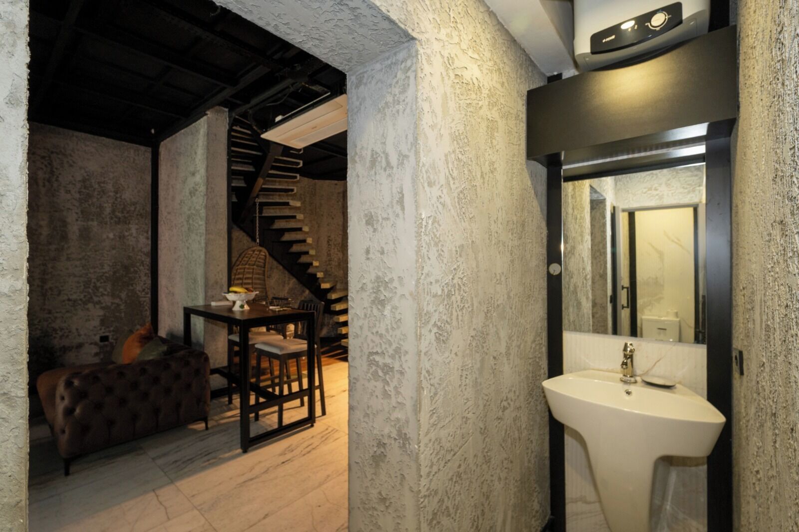 A rustic interior with a staircase, a dining area with a table and chairs, and a bathroom with a sink and mirror.