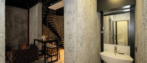 A rustic interior with a staircase, a dining area with a table and chairs, and a bathroom with a sink and mirror.