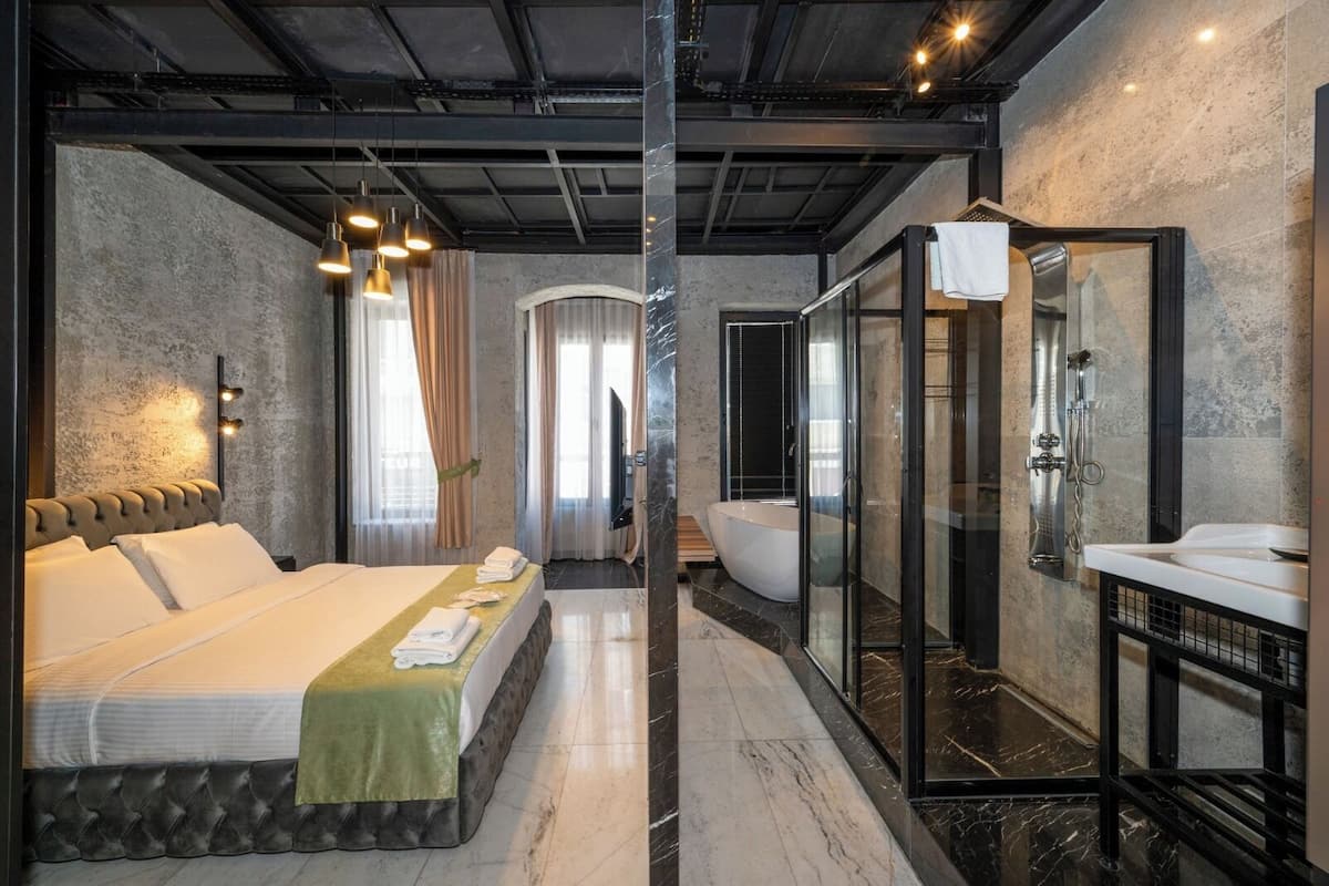 Una habitación de hotel moderna con una cama grande, cabina de ducha y baño con paredes de vidrio.