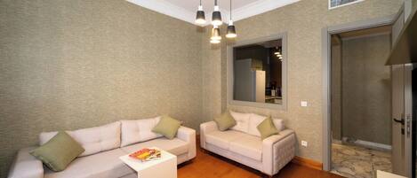 A living room with two sofas, a coffee table, pendant lights, a mirror, and a door leading to a kitchen.