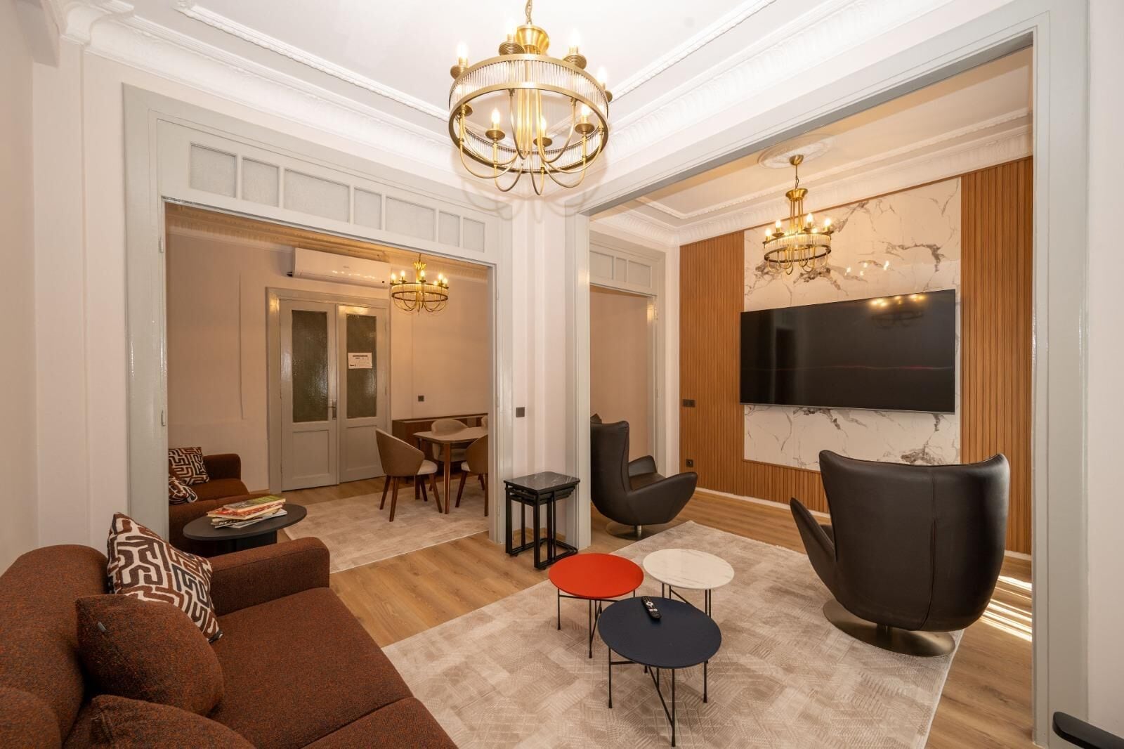 A spacious living area with a sofa, armchairs, a TV, and a chandelier.